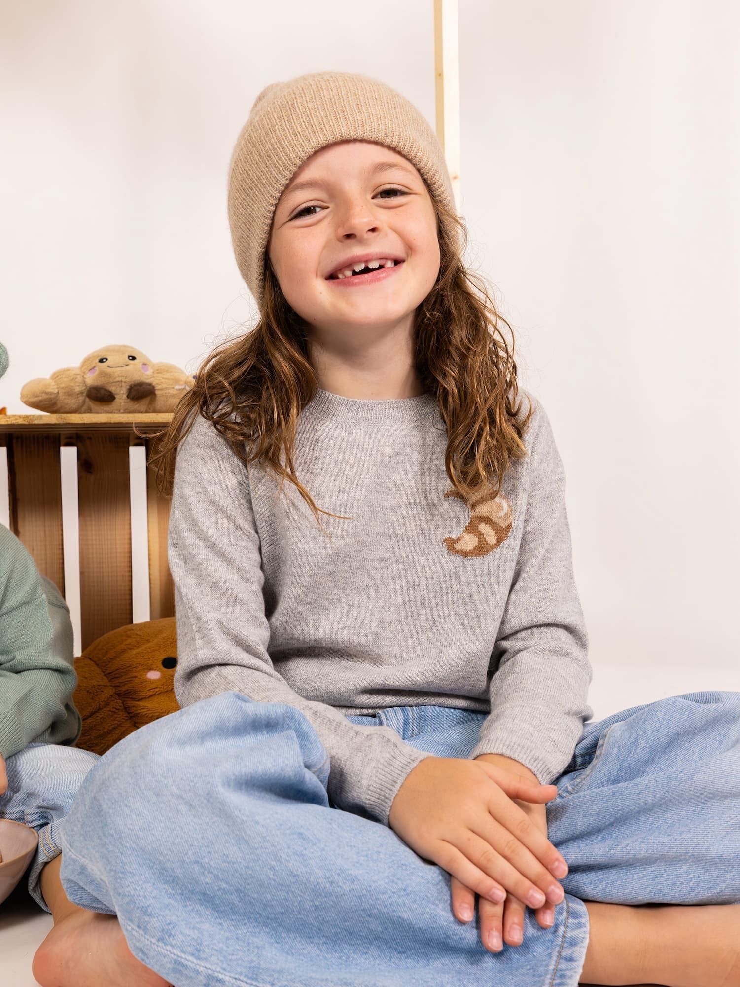 Sitzendes lächelndes Mädchen mit Pullover CROISSANT (Intarsie) und Mütze MALU