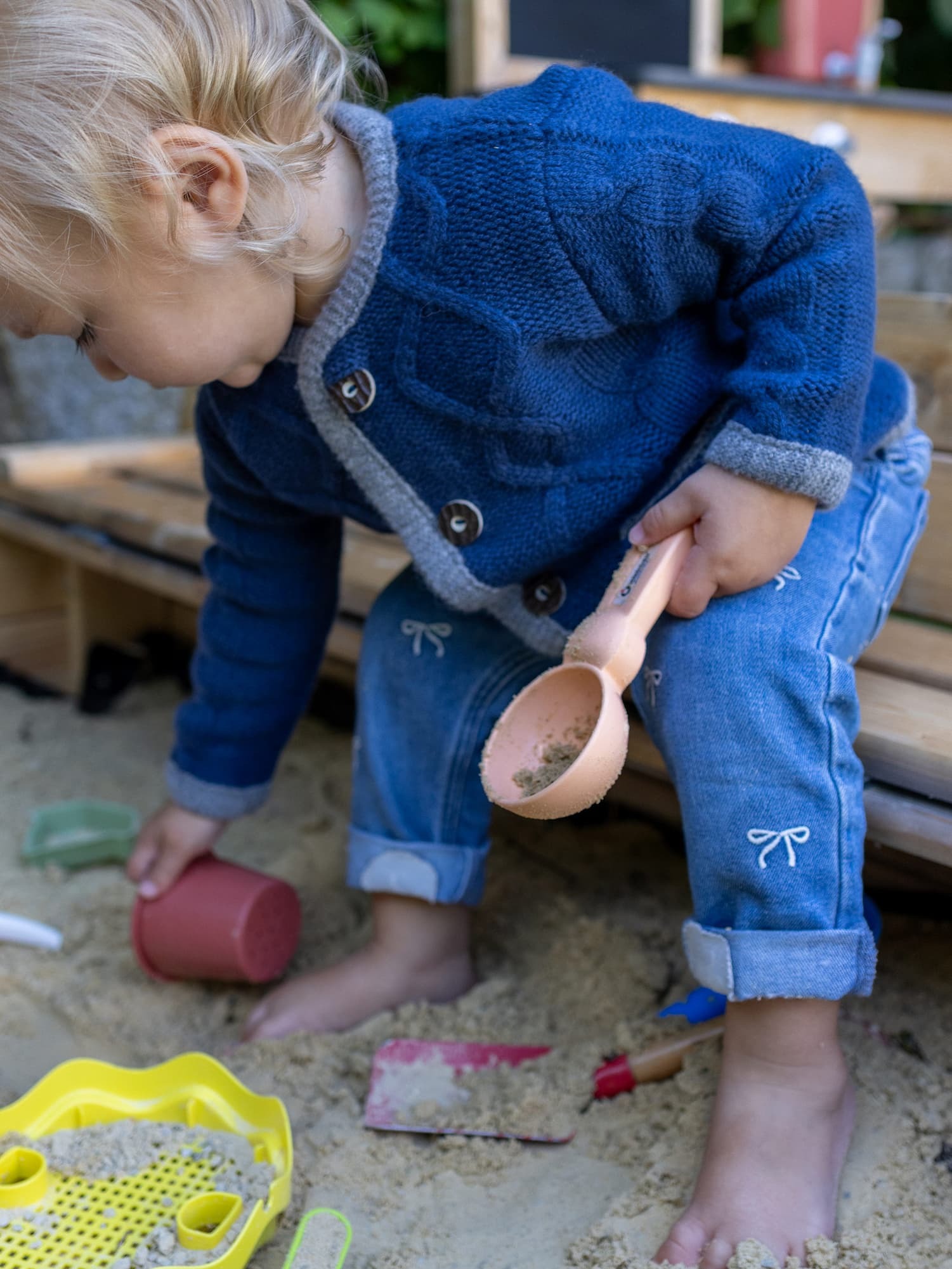 Toddler Mädchen in Kaschmirjacke MAXI und Röckchen sitzt im Sandkasten