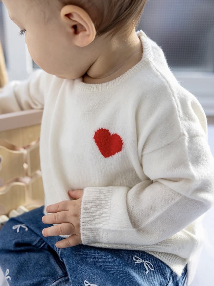 Baby in weißem Kaschmirpullover mit Herz