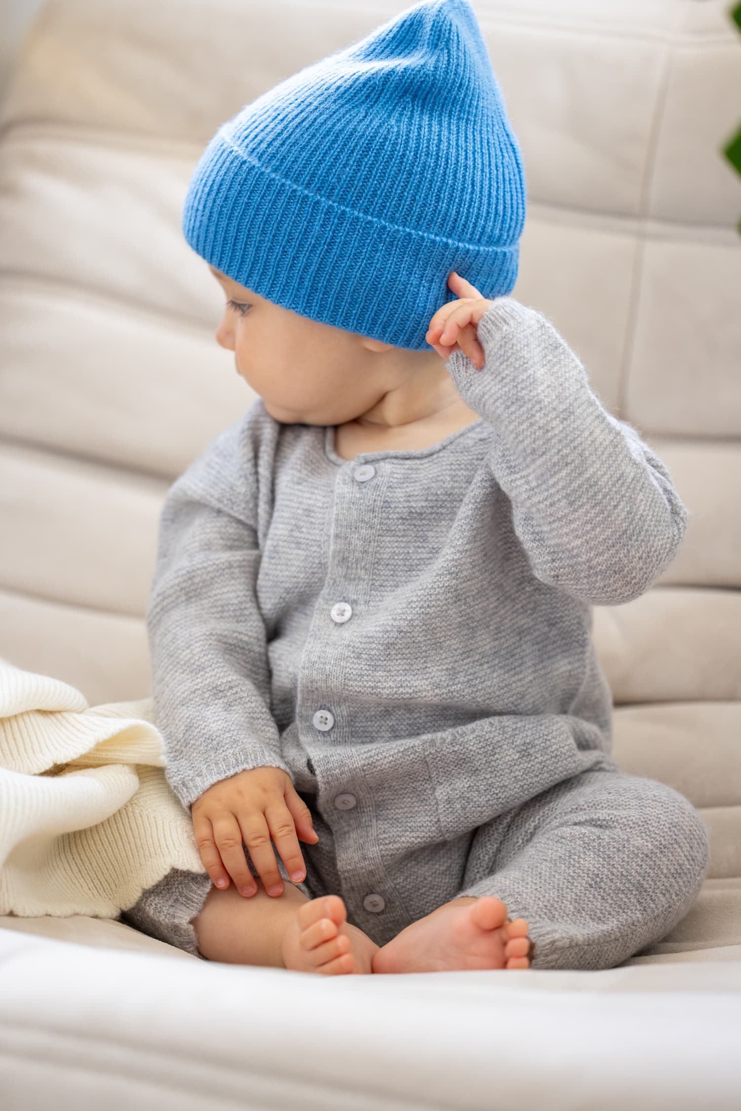 Baby sitzend in Kaschmir Overall ANOUK und blauer Mütze MALU
