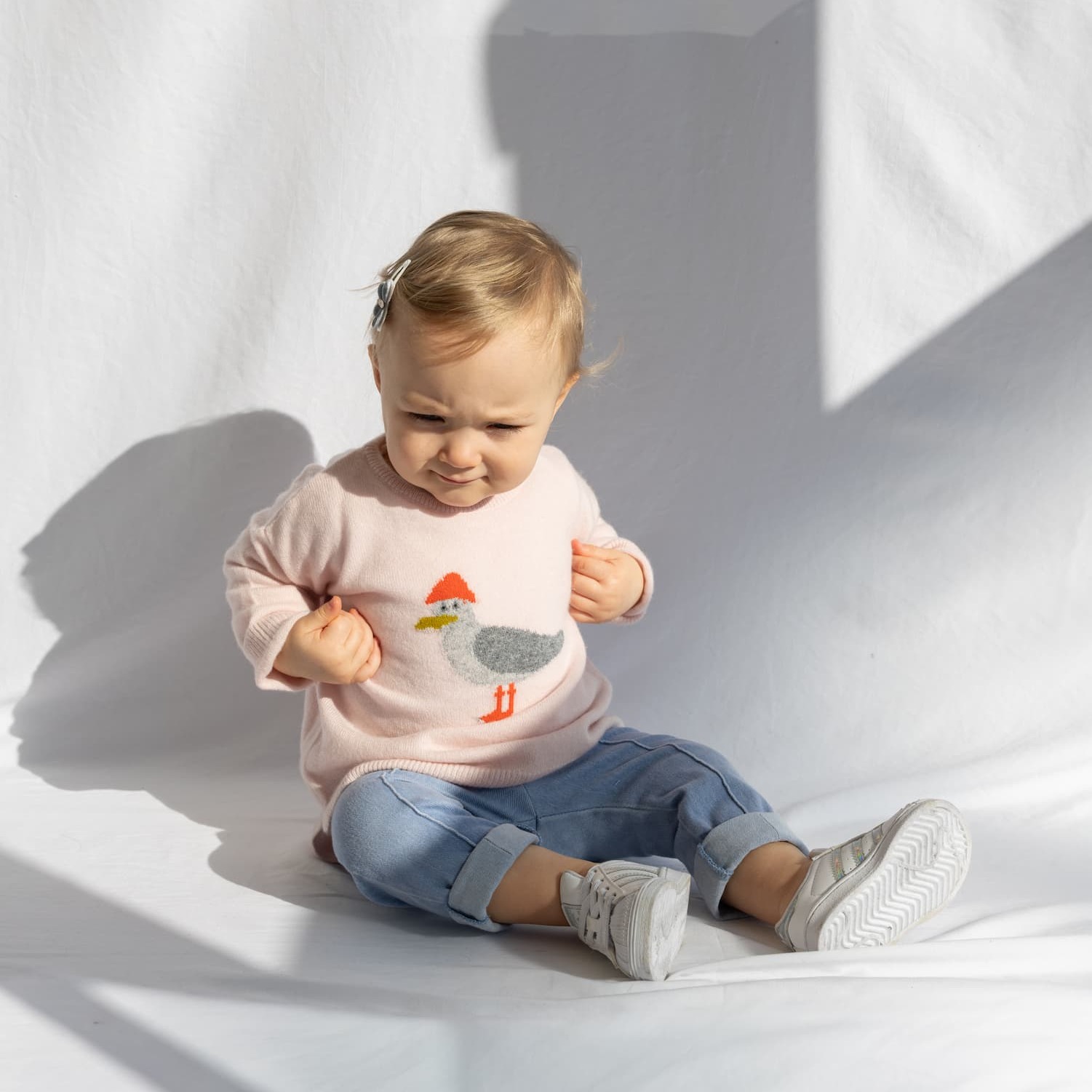 Sitzendes Babymädchen mit Pullover mit Möwen-Intarsie