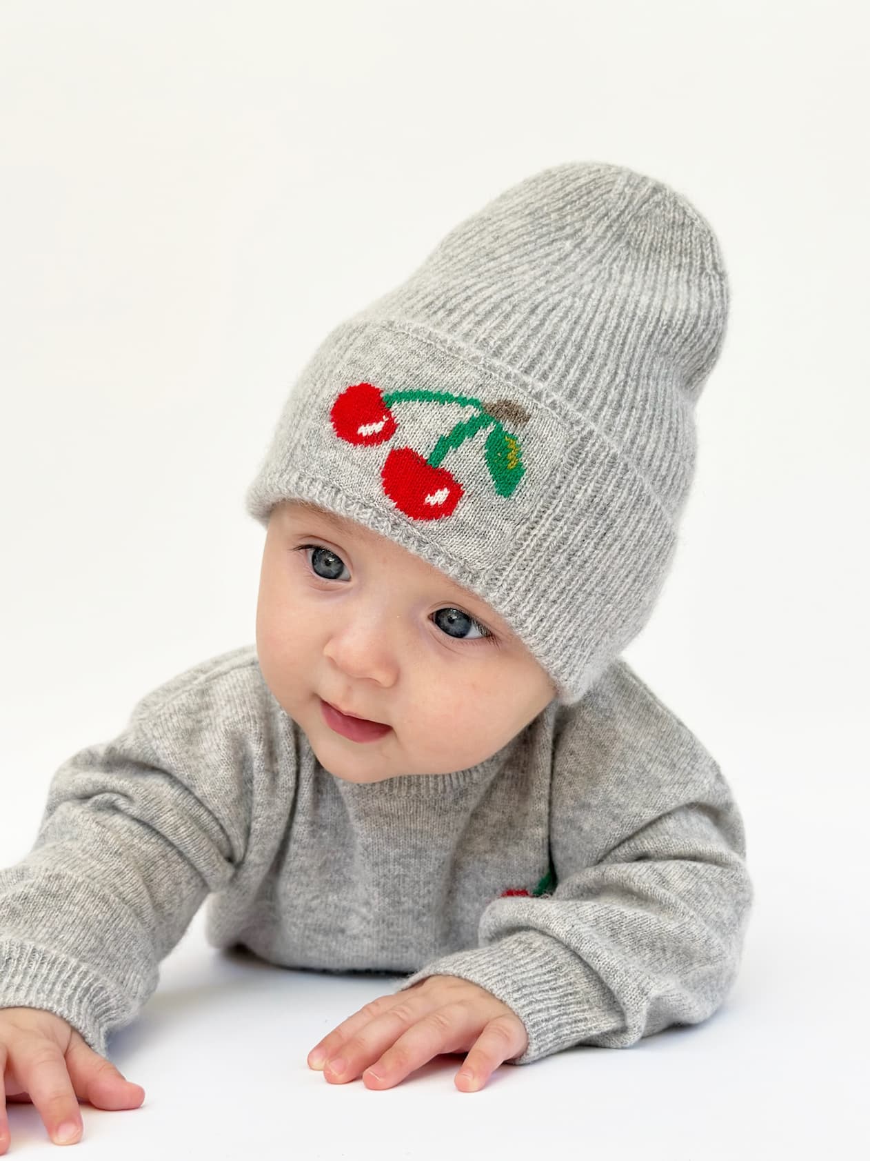 Baby liegend in Pullover und Mütze mit Kirsch-Intarsien