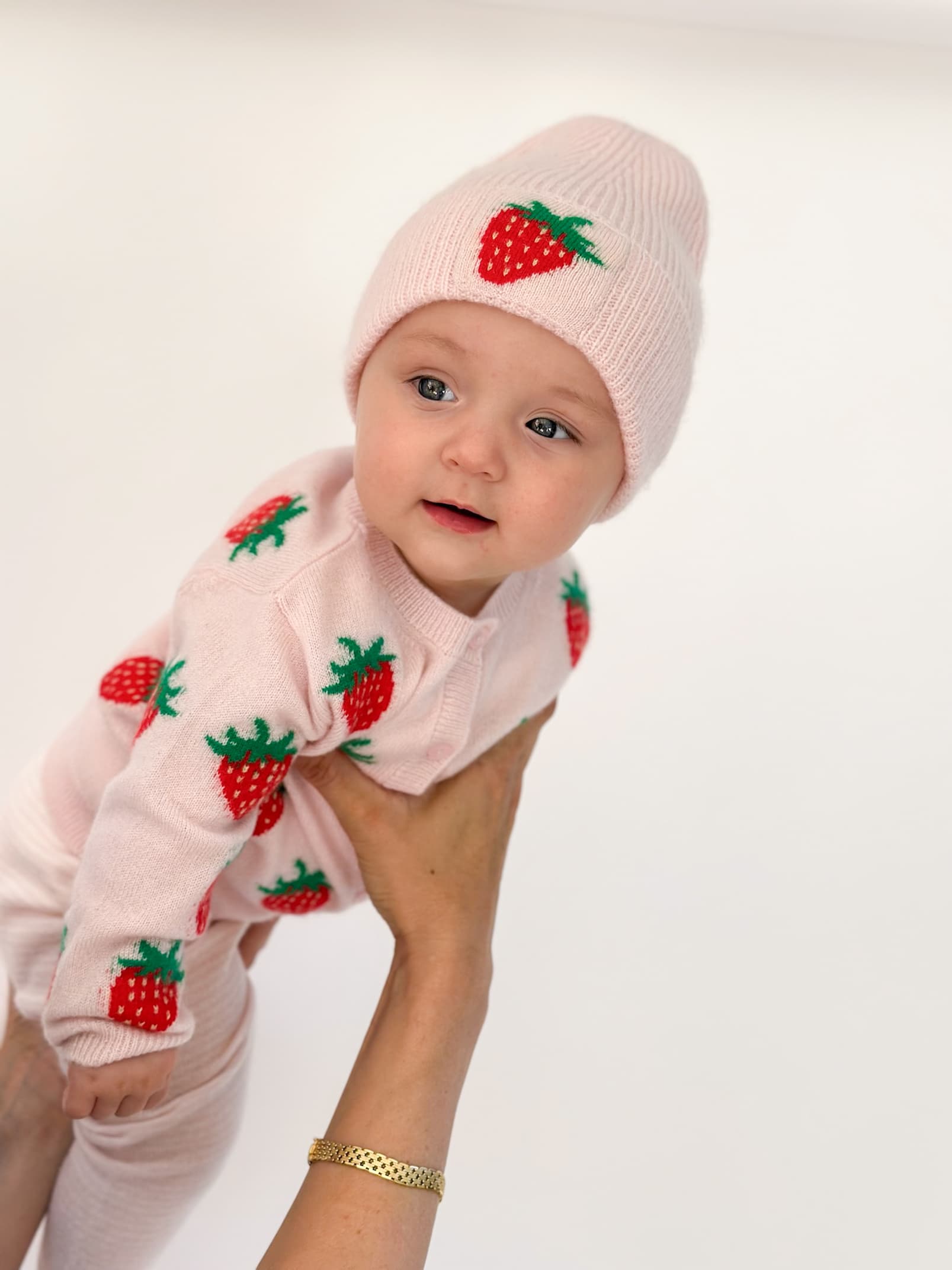Baby in Strickjacke und Mütze mit Erbeer-Intarsien