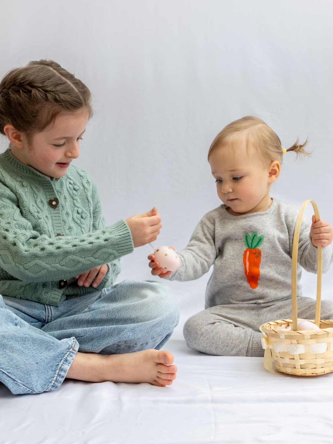 Sitzende Mädchen in Kaschmir-Outfits mit Osterkorb