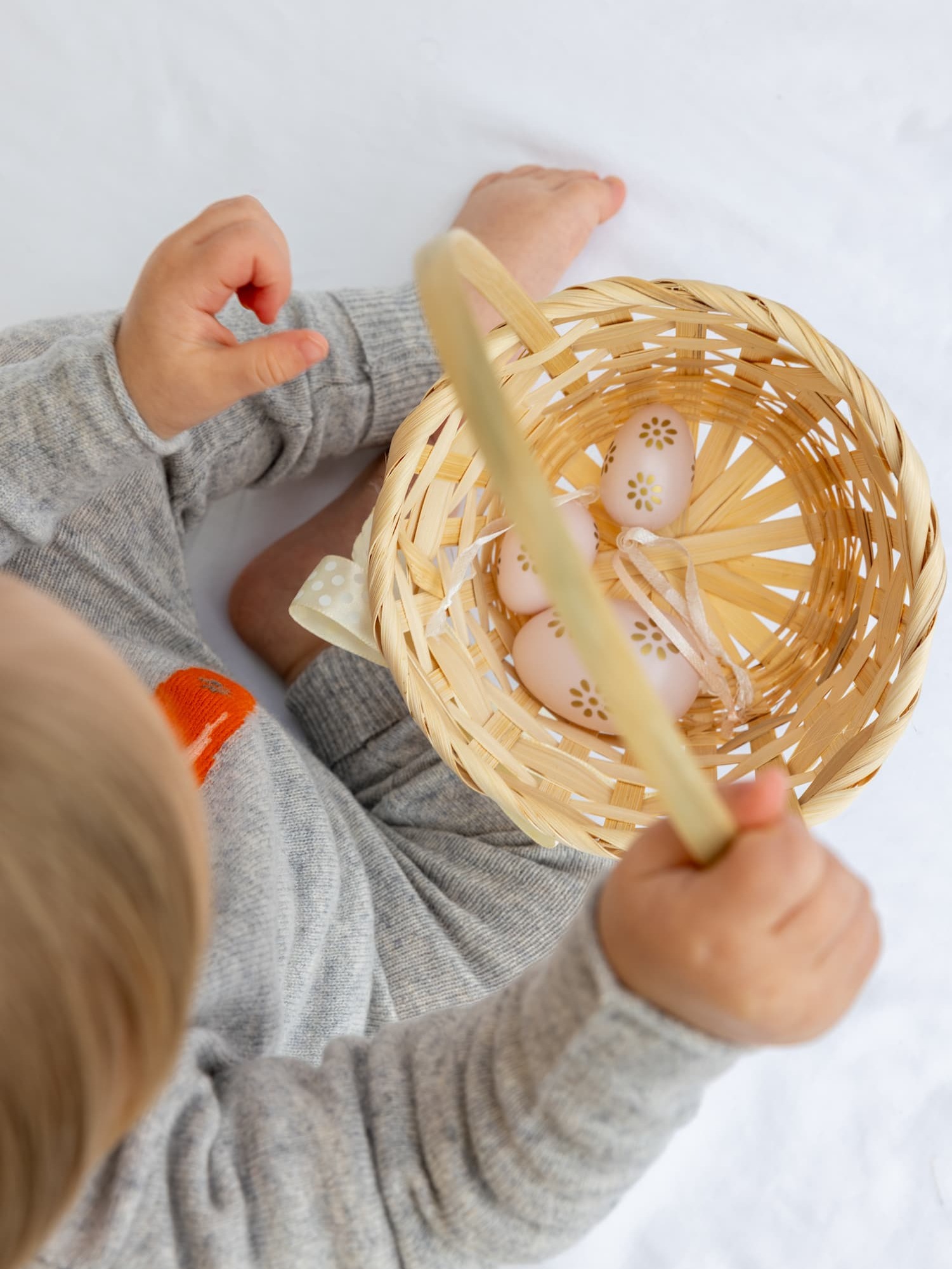 Sitzendes Babymädchen von oben in Kaschmir-Baby-Set mit Karotten-Intarsie und Osterkorb