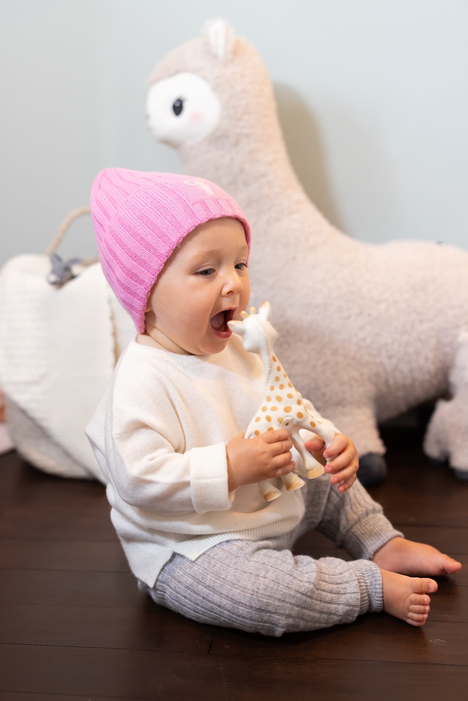 Baby sitzend mit Kaschmirpullover und -hose beisst in Sophie, die Quietschgiraffe