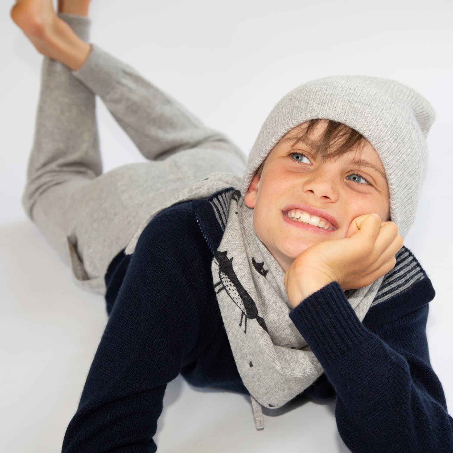 Junge auf Bauch liegend mit Kaschmirhose, -Pullover und Mütze