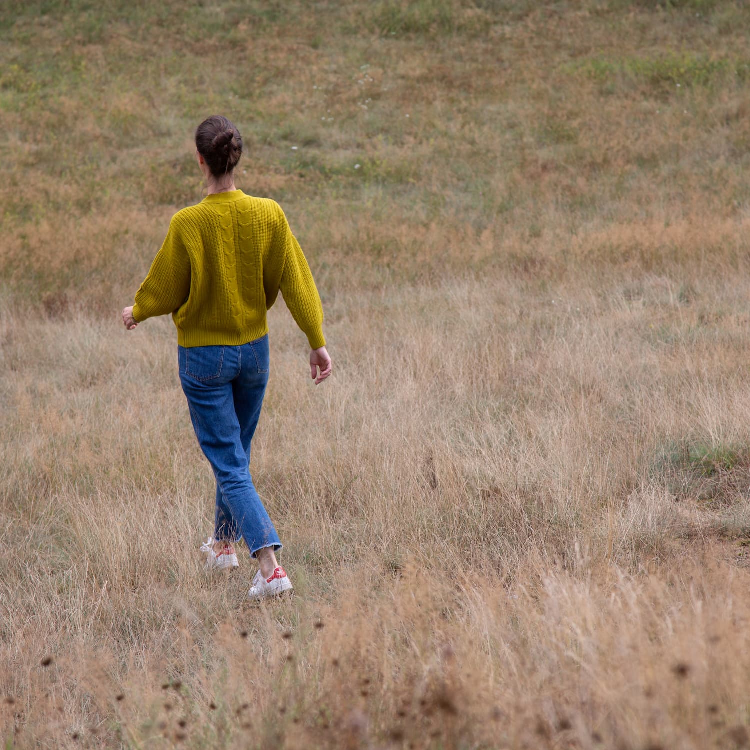 Frau spaziert über herbstliche Wiesenlandschaft