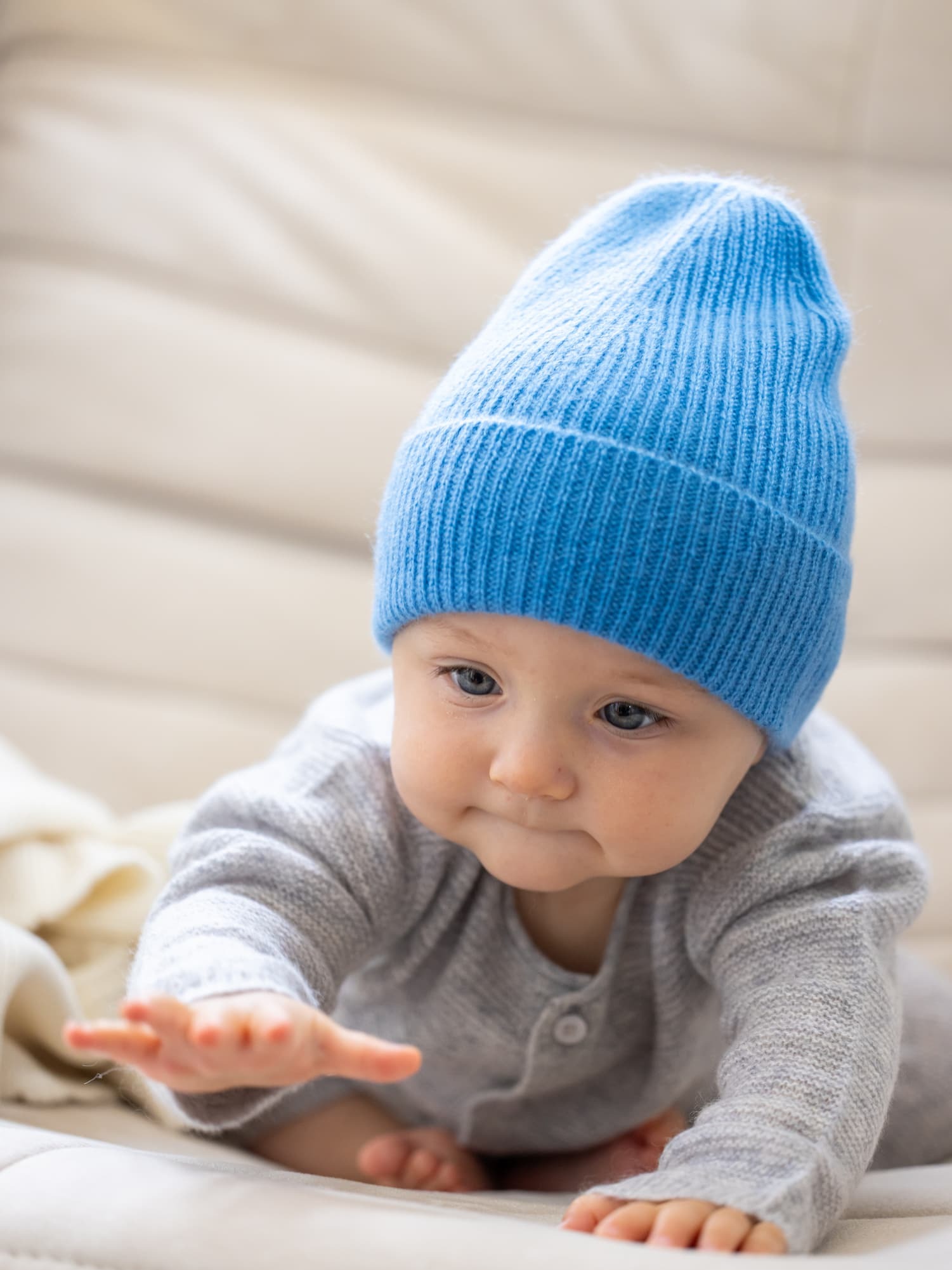 Baby mit Mütze MALU in Ozeanblau beugt sich und greift nach vorne