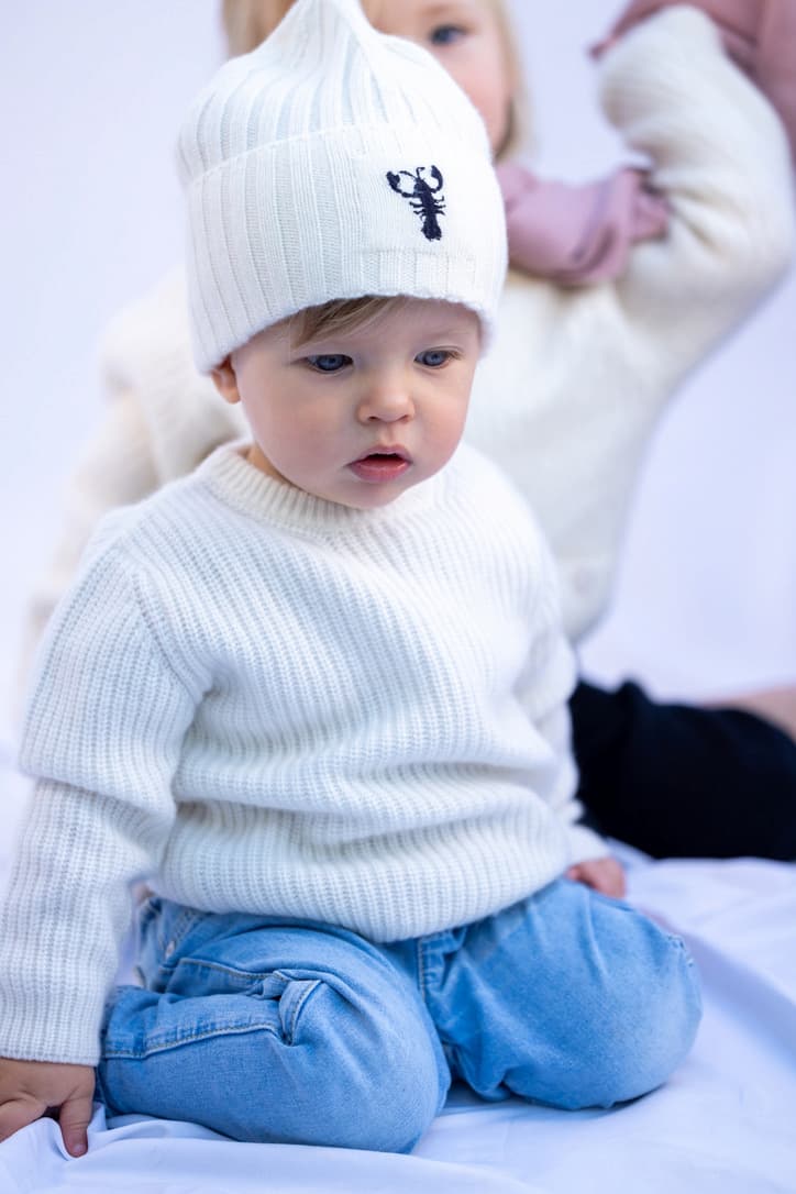 Kleiner Junge sitzend mit Kaschmirpullover und -mütze