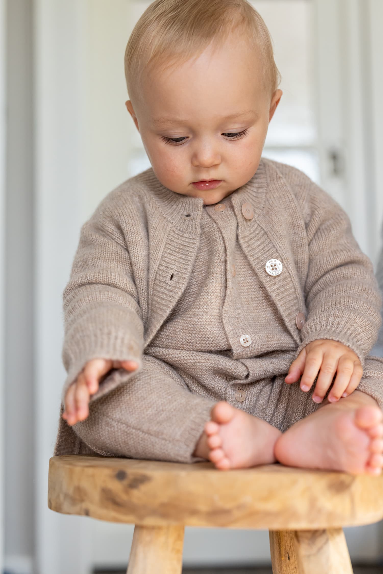 Baby sitzend auf Schemel in beigefarbenem Outfit