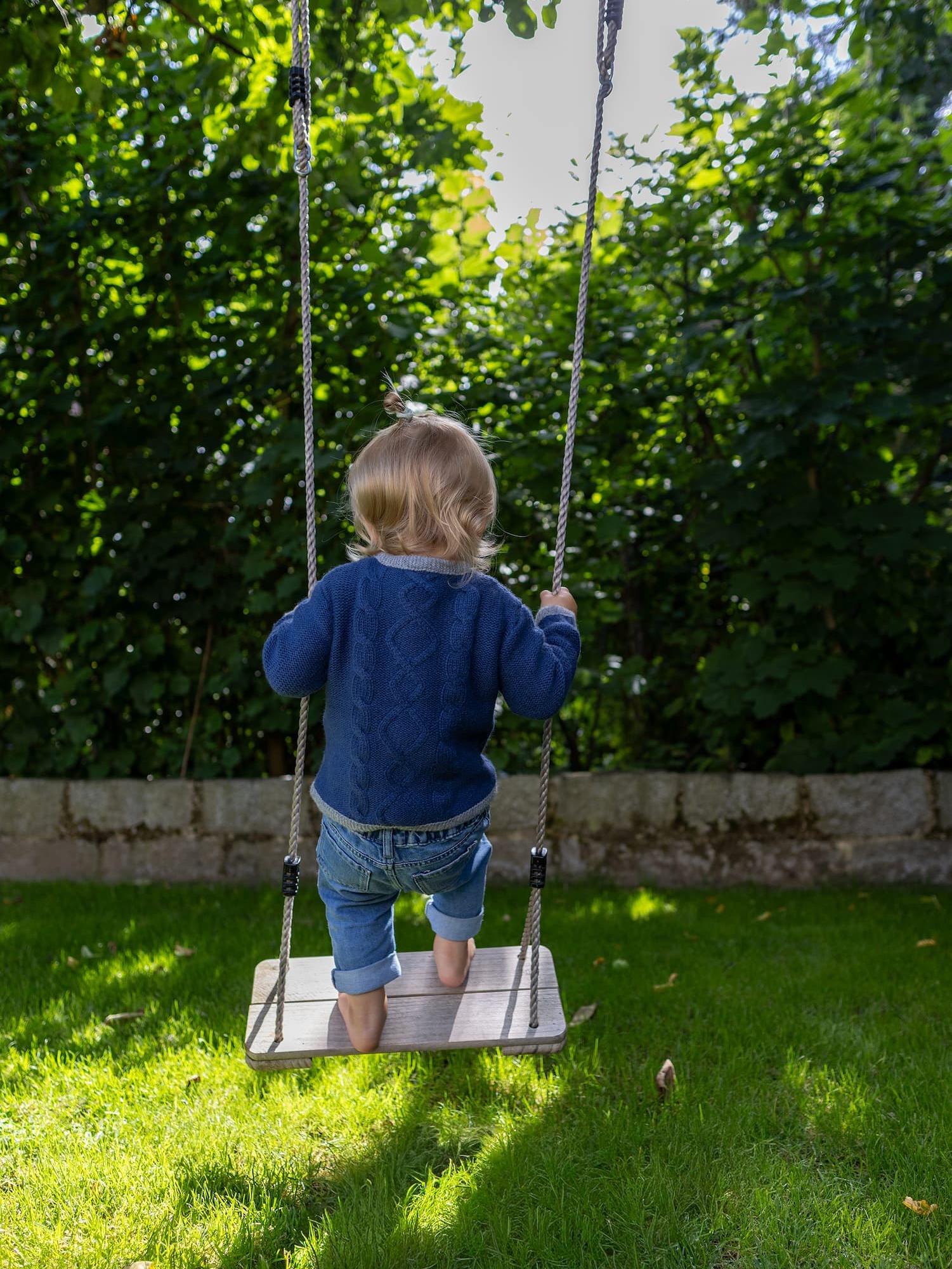 Toddler Mädchen in Kaschmirjacke MAXI steht auf der Schaukel im Garten.