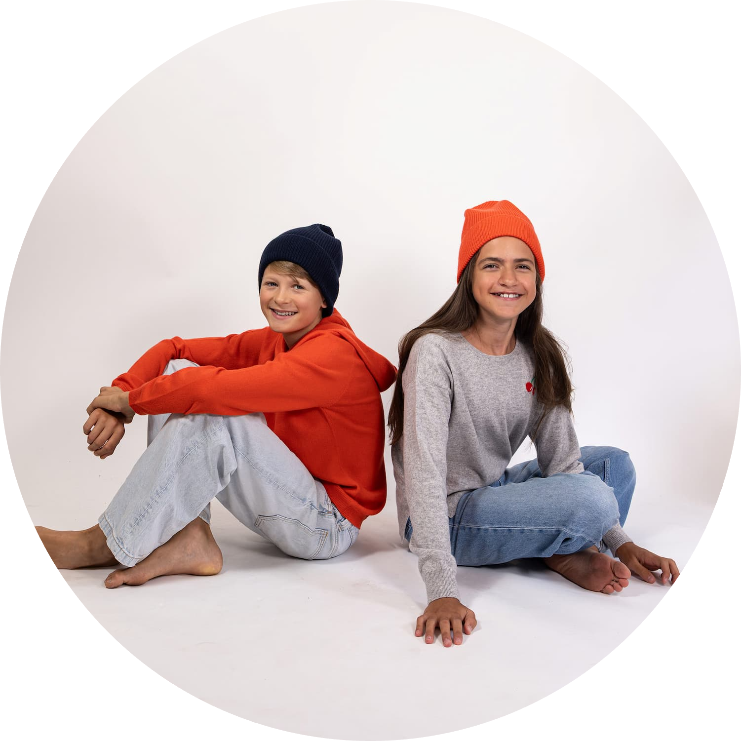Teenie-Junge und -Mädchen sitzend und lächelnd mit Pullover CHERRY, Hoody JONA und Mütze MALU