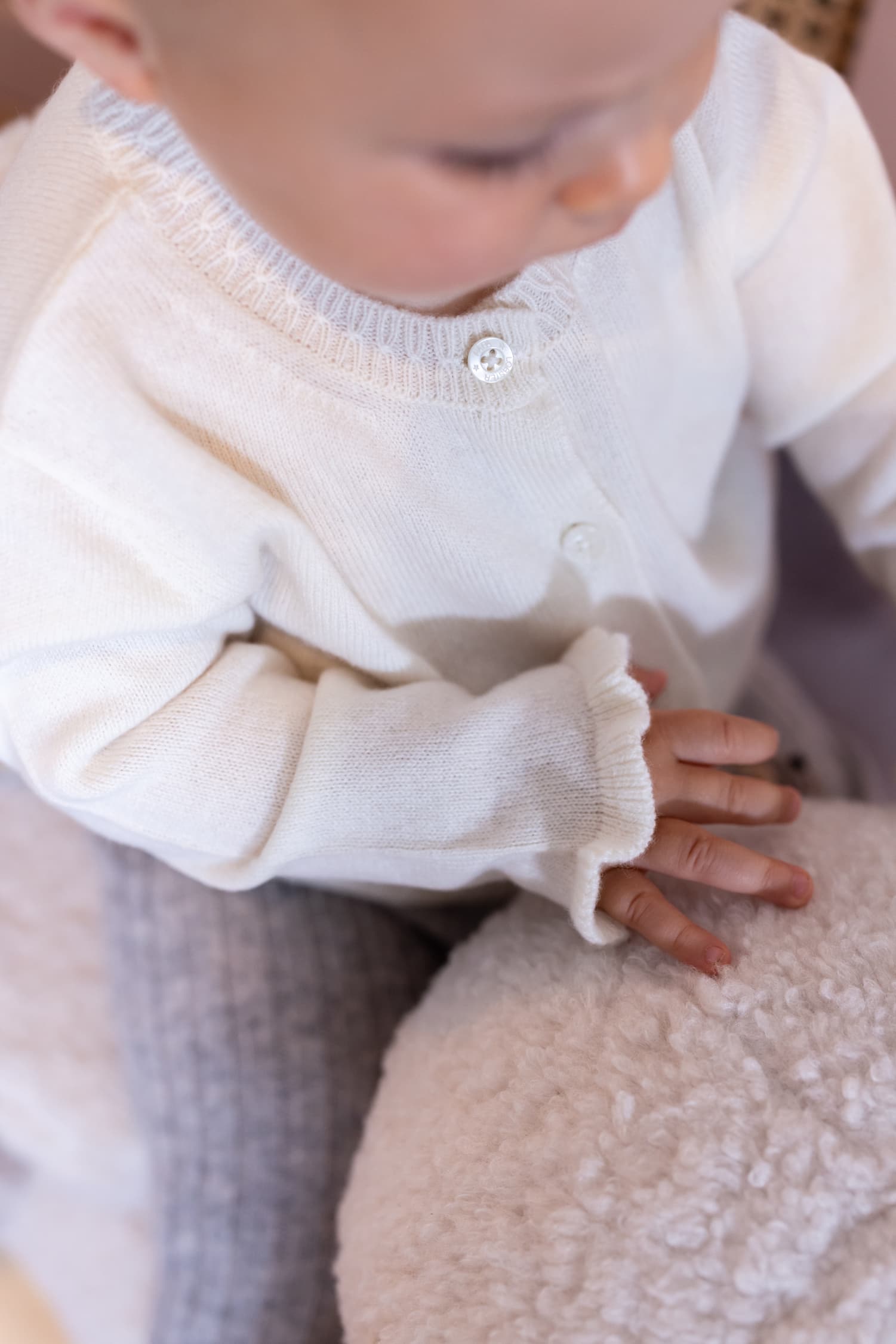 Baby sitzend von oben fotografiert mit weisser Strickjacke SANNA
