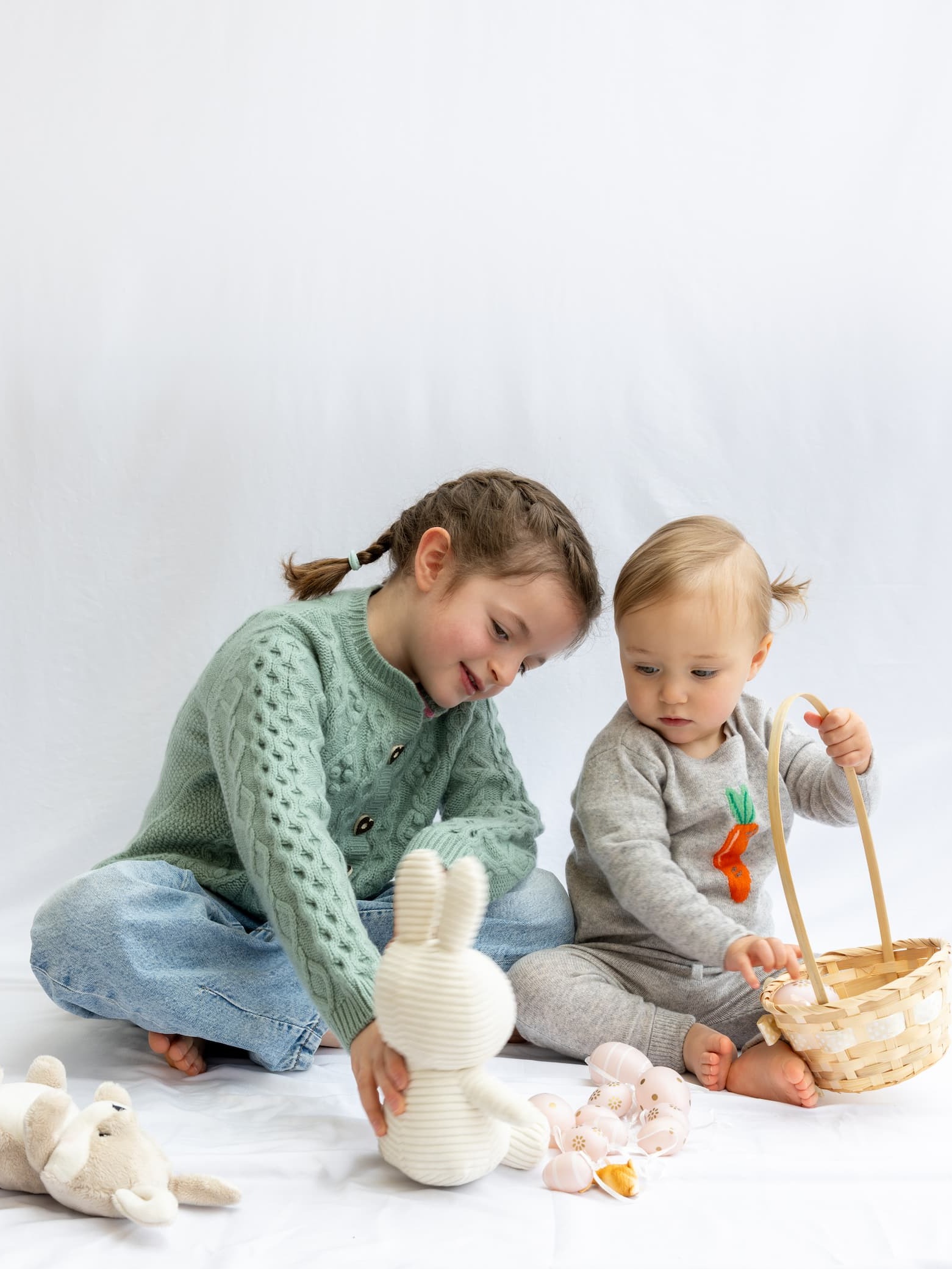 Sitzende Mädchen in Kaschmir-Outfits mit Osterkorb