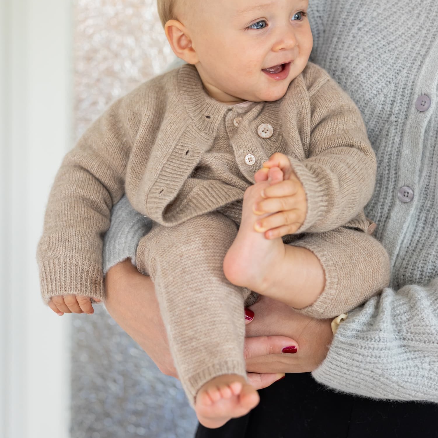 Baby im Arm getragen in beigefarbenen Outfit