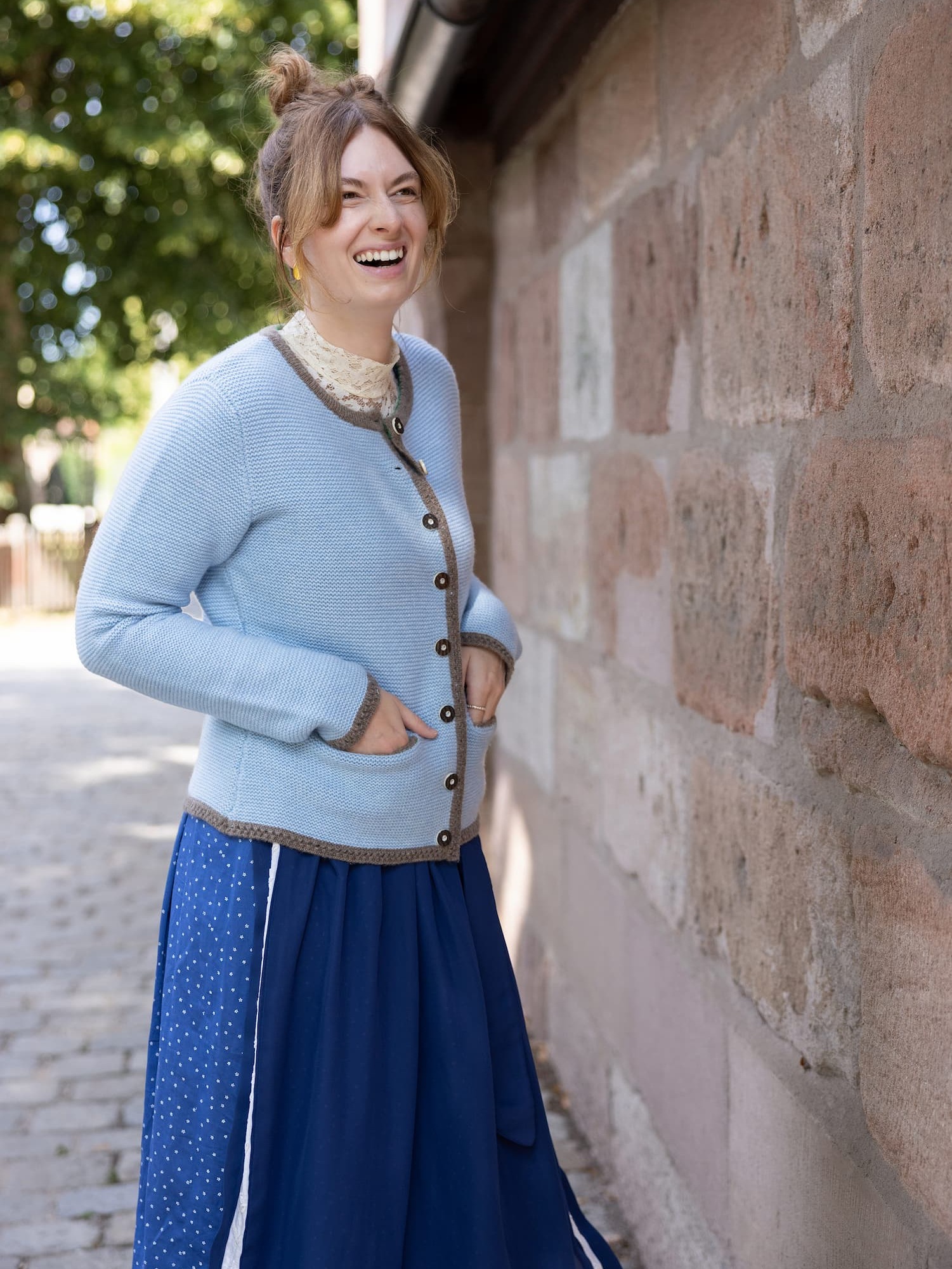 Stehende, lachende Frau mit Cardigan LENI in Hellblau und mit Dirndl