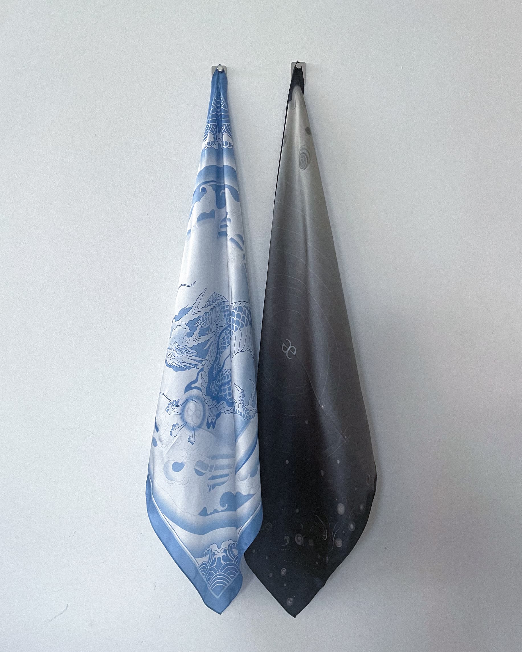 Two Graedance silk scarves hanging against a wall.