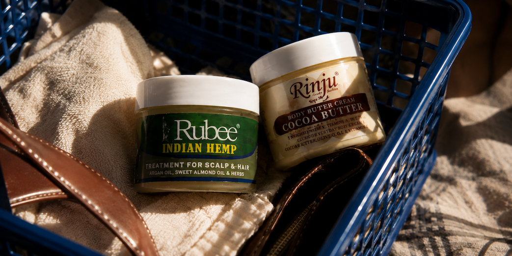 Rubee Indian Hemp and Rinju Cocoa Butter mini jars in a blue basket beside a towel and leather bag