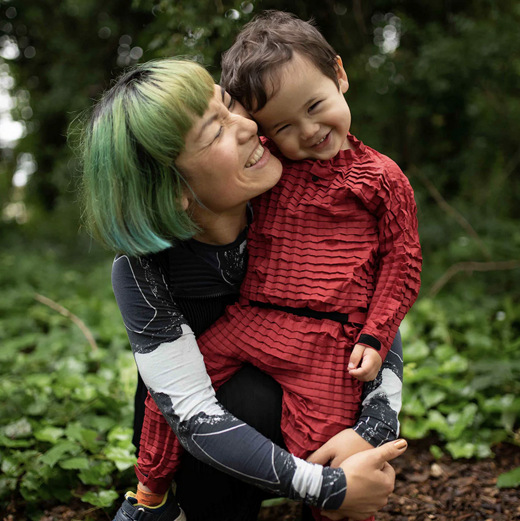 A child in a Petit Pli outfit being hugged by his mum