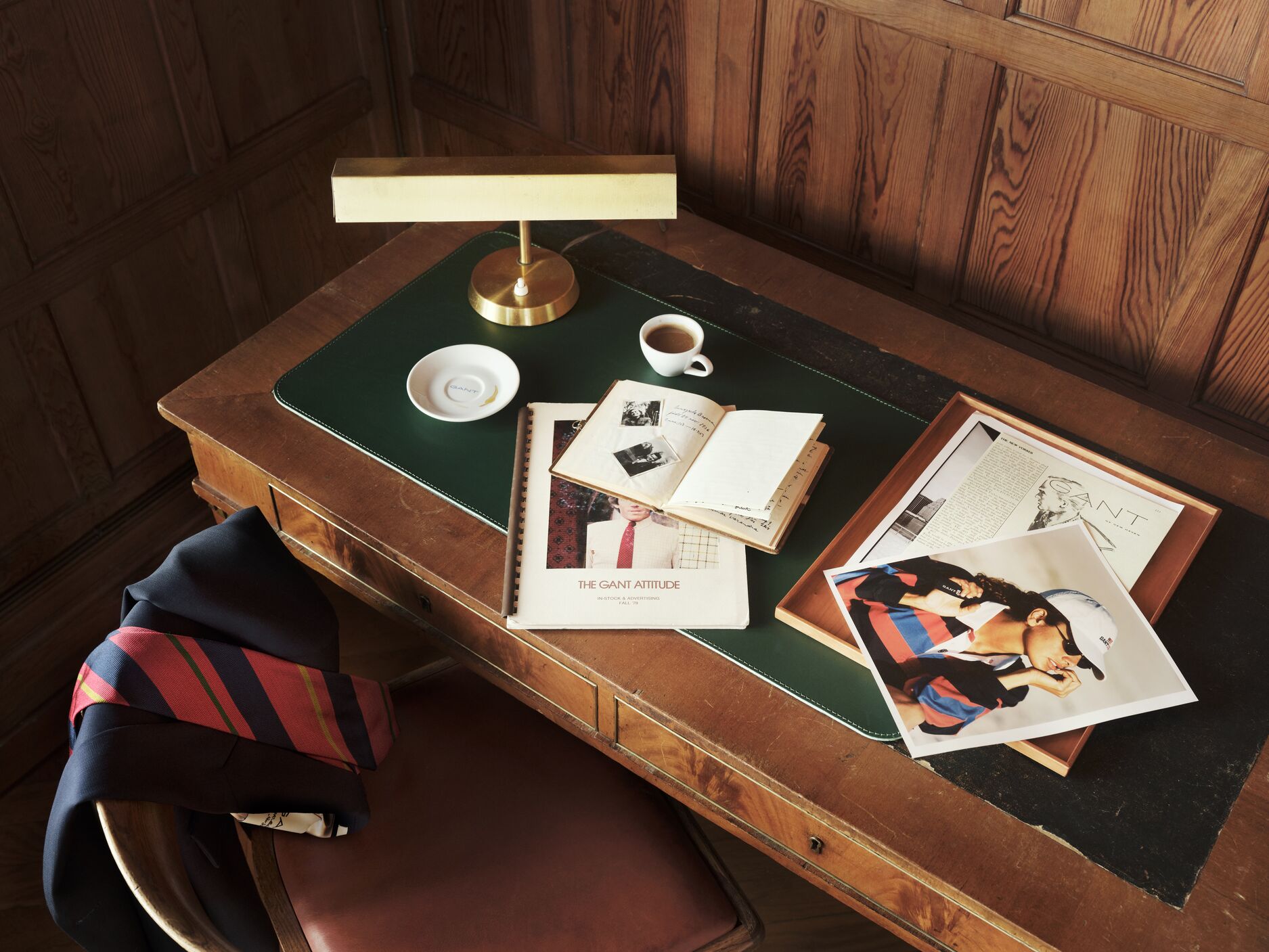 Bilde av et skrivebord med inspirerende magasiner og en stol med en blazer og slips pent hengende over. 