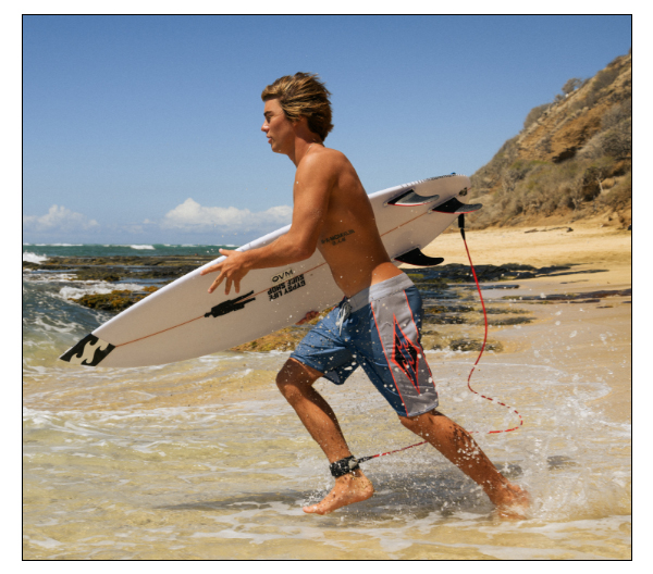 Billabong male surfer running into the ocean with a surfboard.