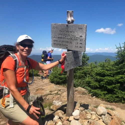 a hiker sits beside a sign on a mountaintop