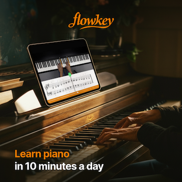 Closeup of hands playing a piano with the flowkey app open on a tablet