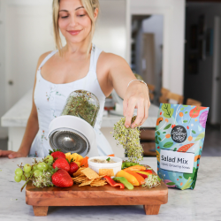 A woman with a sprouting kit and a spread of fruits and veggies.