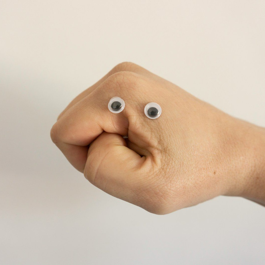 A person's fist making a mouth shape and wearing googly eyes