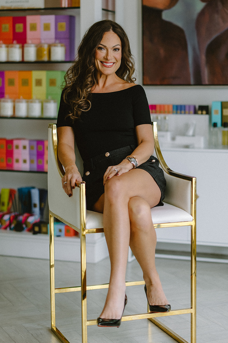 Diana Shelton-Flanary, owner of POUT Cosmetics & Skin Studio, seated in a gold chair in the studio