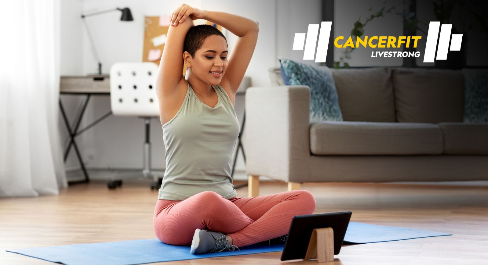A young woman stretching on a yoga mat following a workout video on a tablet
