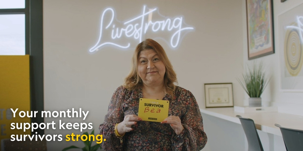 A woman holding a yellow card in front of a Livestrong neon sign