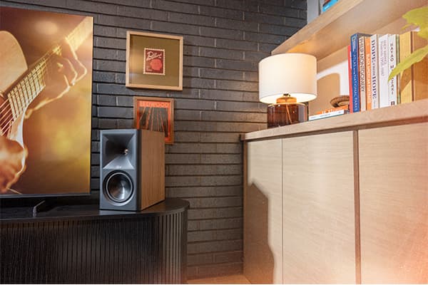 Walnut finished Klipsch Fives II bookshelf speaker sitting on a dark tv cabinet in a stylish modern living room