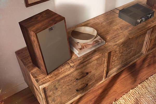Top view of a Tigerwood Klipsch Rebellion speaker, sitting on a wooden cabinet, in a modern living room.