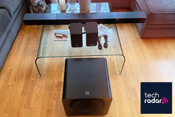 Klipsch Flexus sound bar, surround speakers, and subwoofer on and around a glass table.
