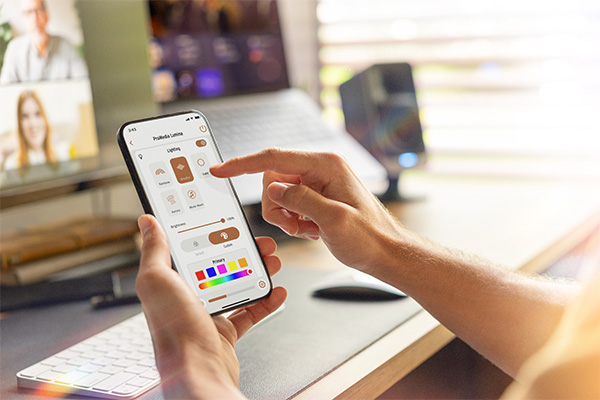 Image of someone using the Klipsch mobile app on their smartphone, with a modern desktop computer and speakers in the background.