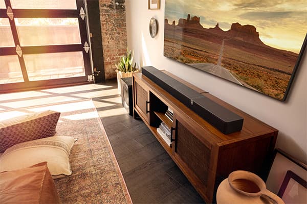 Klipsch Flexus Core 300 sound bar sitting on a wooden cabinet, under a flat screen tv, in a warmly lit living room.