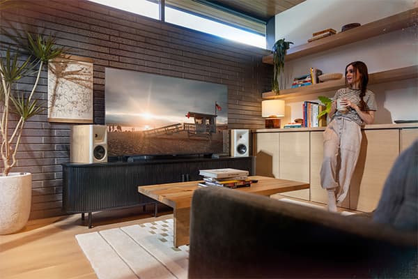 Young young with a coffee mug listening to Red Oak Klipsch Fives II speakers in a stylish living room
