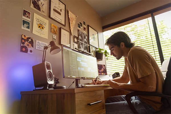 Young man working at his computer desk, with a pair of Klipsch ProMedia Lumina speakers on both sides of his desktop computer