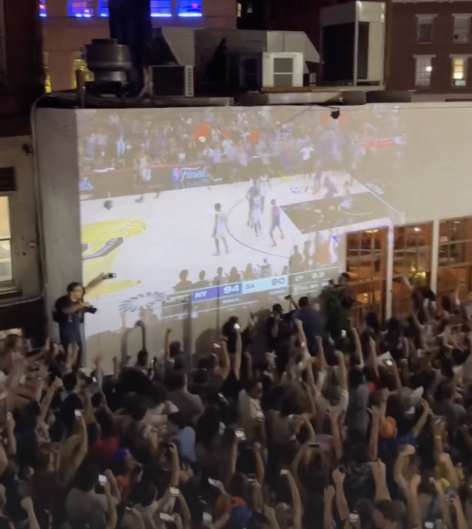 A packed crowd watching the Knicks championship game on a giant outdoor screen in New York City