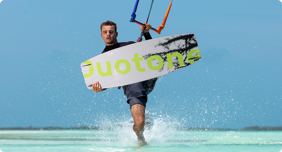 Kitesurfer carrying a lime Duotone twintip at the water’s edge