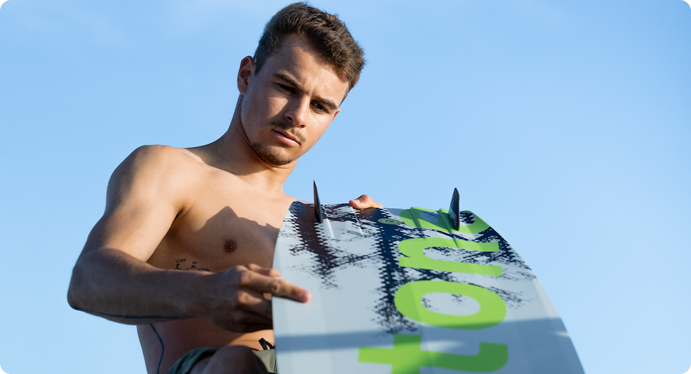 Rider holding a lime Duotone board on a bright tropical beach