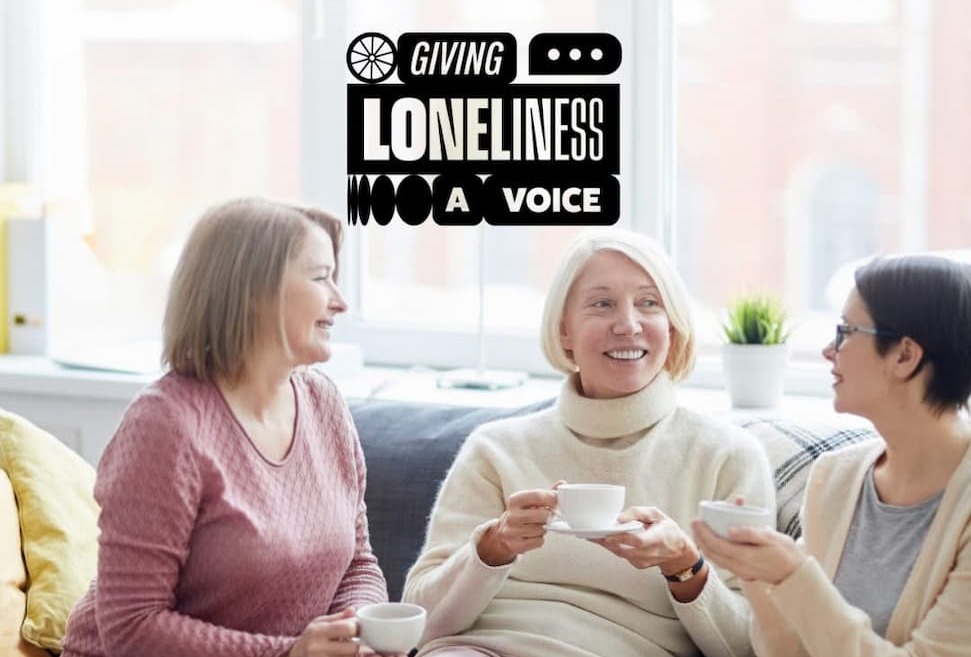 Three women smiling and sharing a chat over a brew with the slogan 'Giving Loneliness a Voice'