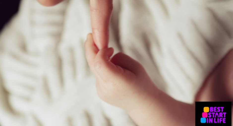 A tiny baby's hand clasping an adult finger