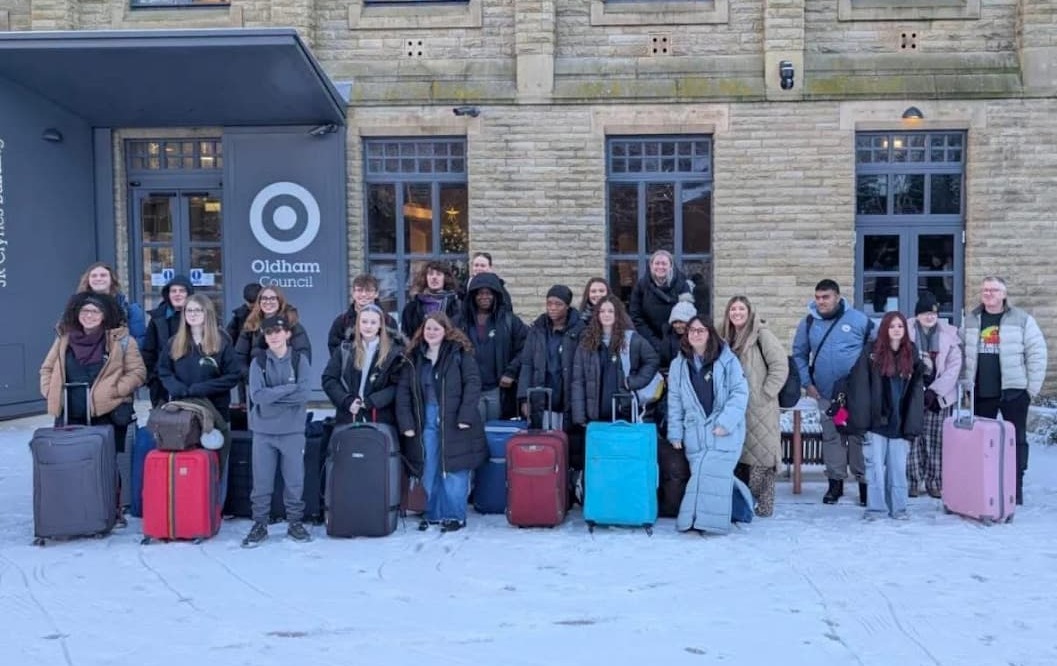 A group of young people smiling with suitcases in front of an Oldham Council signas they head off on their journey to  Auschwitz-Birkenau 