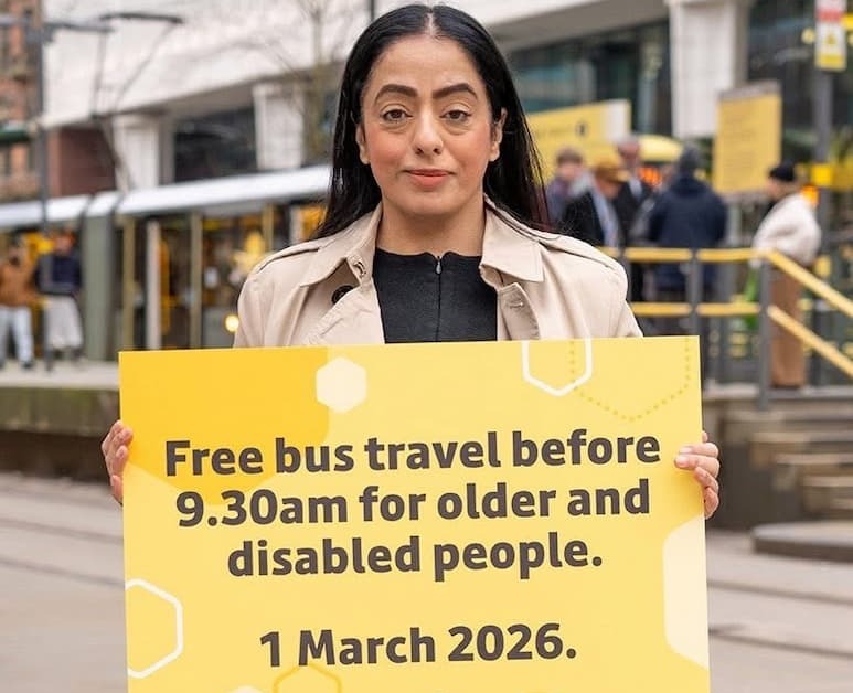 Cllr Arooj Shah next to a tram stop in Manchester city centre holding a sign reading 'Free bus travel before 9.30am for older and disabled people. 1 March 2026.'