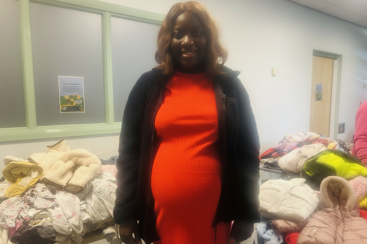 An expectant mum smiling into the camera with a collection of donated clothes behind her