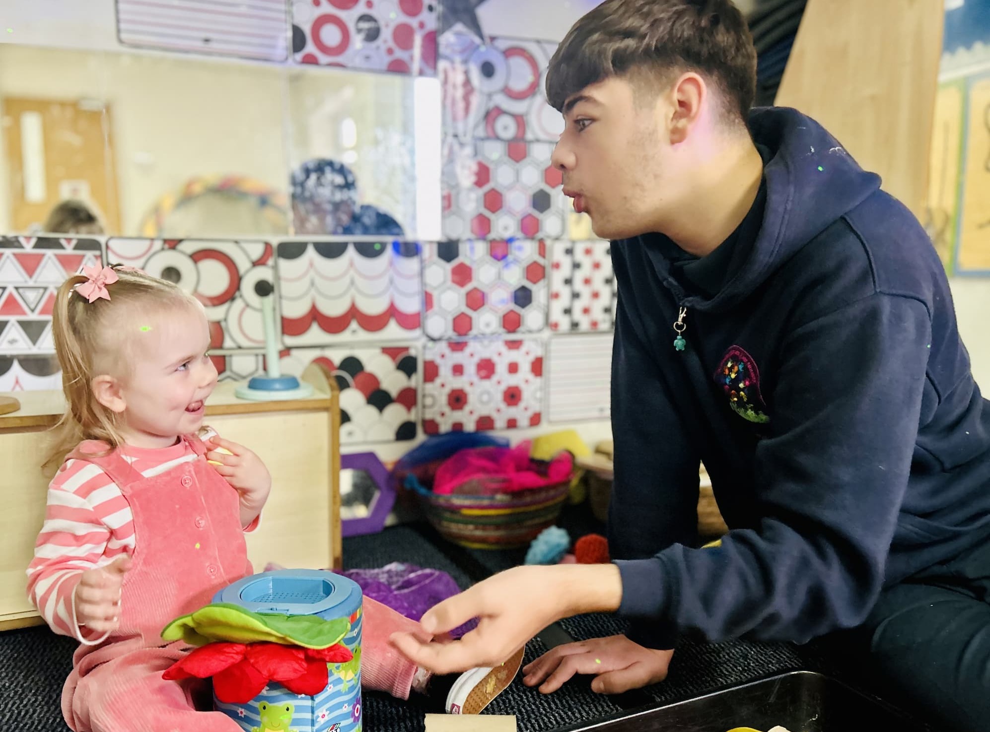 Apprentice Harley working at Buttercup Corner Day Nursery, smiling and engaging in play with one of the children