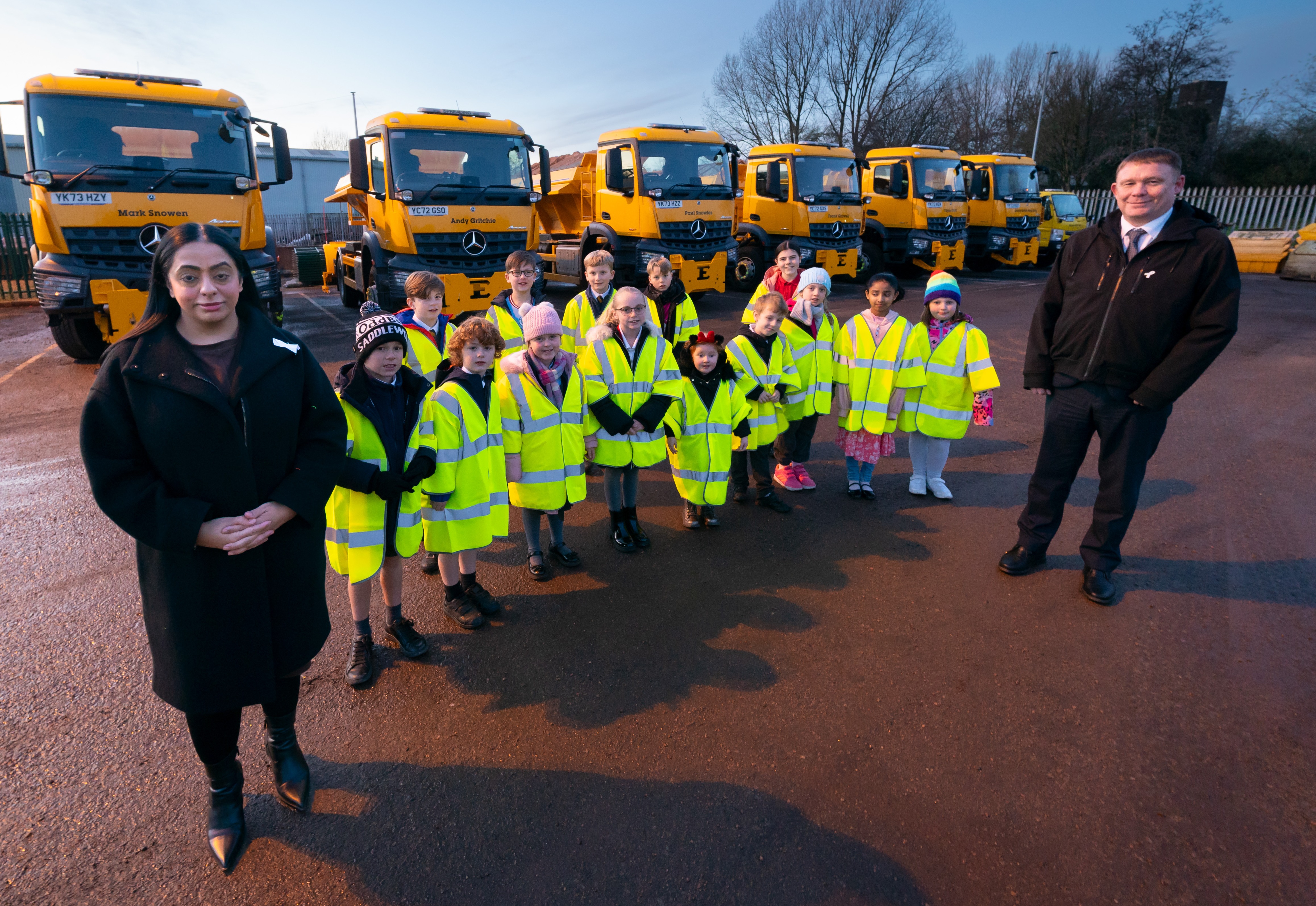 Oldham's school children standing in front of the newly named gritters with Cllr Shah and Cllr Goodwin.